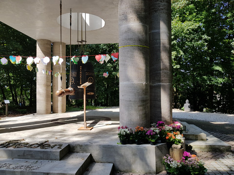 Garten des Buddhistischen Zentrums Offener Pavillon im Wald mit Glocke und Blumen, dekoriert mit hängenden Papierlaternen und Herzen.