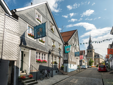 Hückeswagen Fachwerkhäuser mit bunten Fahnen in Hückeswagen, Kopfsteinpflasterstraße und Kirchturm im Hintergrund.