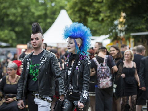 Dwie osoby z irokezami i w skórzanych kurtkach przechodzą przez tłum na festiwalu punkowym.