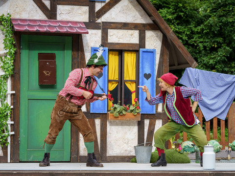 Neues_vom_Räuber_Hotzenplotz_Foto-Dirk-Rückschloss.jpg Zwei Schauspieler in traditioneller Kleidung posieren auf einer Bühne vor einem märchenhaften Haus.