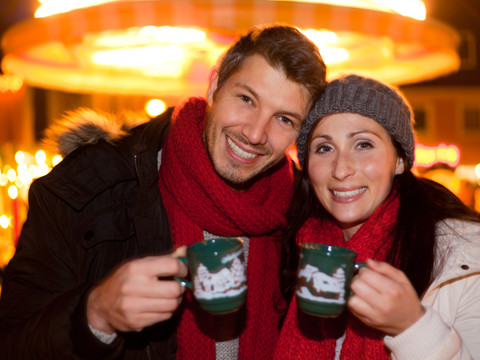 Glühwein Junges Paar in Winterkleidung hält Becher mit heißen Getränken auf einem festlichen Markt.