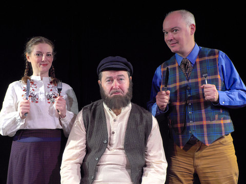 TEVYE MELF9913.JPG Drei Schauspieler in traditionellen Kostümen auf einer schwarzen Bühne posieren fröhlich.