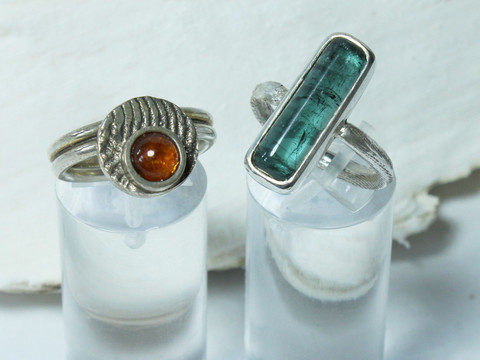 Links ein Ring mit einer runden Scheibe und einem orangen Edelstein und rechts daneben ein Ring mit einem länglichen blauen Edelstein von Sarah Gaus im Palmendieb Atelier Leipzig, regionale Produkte