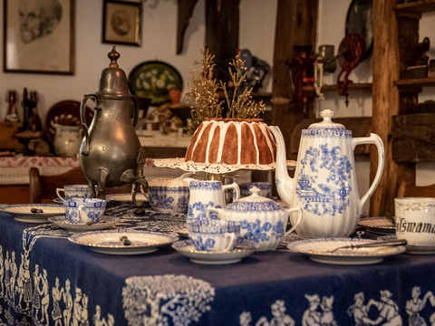 Heimatmuseum  Ein gedeckter Tisch mit blau-weißem Porzellan, einer Kaffeekanne und einem Gugelhupf im Vintage-Stil.