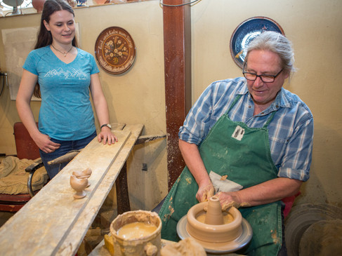 Mann töpfert, während Frau interessiert zuschaut; traditionelle Handwerkskunst.