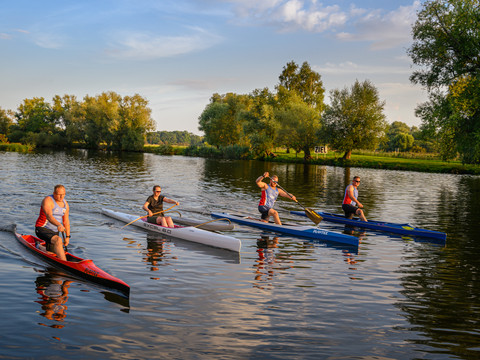 Paddling on the Mulde © WelterbeRegion Anhalt-Dessau-Wittenberg e.V., Uwe Weigel, 2021 (2).jpg Vier peddelaars bij een oever, omringd door bomen, peddelend op een kalm rivieroppervlak.
