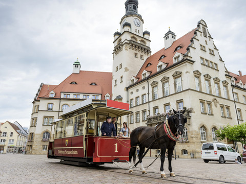 Kolej konna w Döbeln © Christian-Hüller-Fotografie_region.leipzig (25).jpg Zabytkowa kolejka konna z maszynistą przed dużym starym budynkiem w tle.