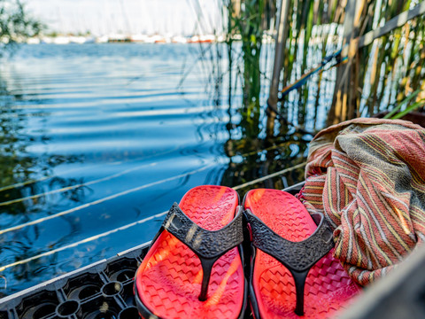 Wassereinstieg Sauna im See - Wellness in Leipzig und Region Zwei Flipflops in Nahaufnahme und daneben liegendem Badetuch am Wassereinstieg des Sees mit Schilf und Booten im Hintergrund