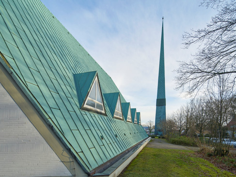Eine moderne Kirche mit markantem grünen Dach und schlankem Kirchturm in einer Parklandschaft in Osnabrück.