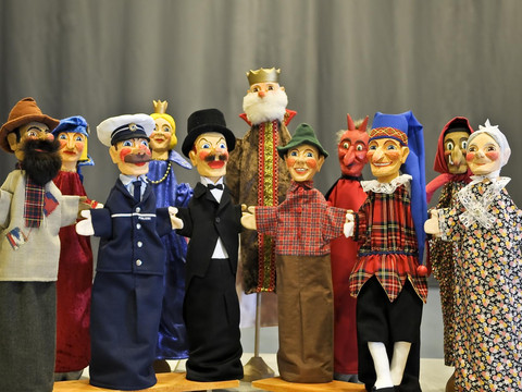 Punch and Judy Puppets from the Max Jacob Theatre Eine Gruppe bunter Handpuppen, darunter ein Polizist, ein König und ein Teufel, vor einem grauen Hintergrund. Die Puppen tragen fröhliche Gesichtsausdrücke.