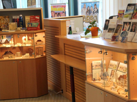 Empfangstresen im Tourismus Servicezentrum Neustadt in Sachsen Holzvitrine in einem Geschäft mit Souvenirs, Miniaturmodellen und Broschüren; daneben ein Tresen mit Prospekten und einer Topfpflanze.Wooden display case in a store with souvenirs, miniature models and brochures; next to it a counter with brochures and a potted plant.Dřevěná vitrína v obchodě se suvenýry, miniaturními modely a prospekty; vedle ní pult s prospekty a květináčem.Drewniana gablota w sklepie z pamiątkami, miniaturowymi modelami i broszurami; obok lada z broszurami i rośliną doniczkową.Houten vitrinekast in een winkel met souvenirs, miniatuurmodellen en brochures; daarnaast een toonbank met brochures en een potplant.Vetrina in legno in un negozio con souvenir, modellini e opuscoli; accanto un bancone con opuscoli e una pianta in vaso.