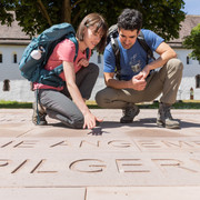 Höxter-Brenkhausen-Kloster-Teutoburger-Wald-Tourismus-A-Röser-042.jpg Zwei Wanderer betrachten Schriftzüge auf einer Steinplatte vor einem historischen Klostergebäude.