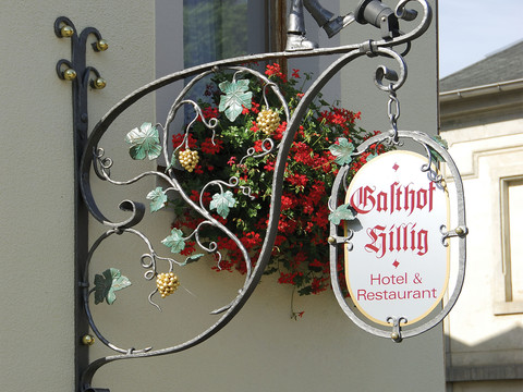 Gasthof Hillig Schmiedeeisernes Schild mit bunter Blumenpracht, präsentiert Gasthof Hillig, Hotel und Restaurant.