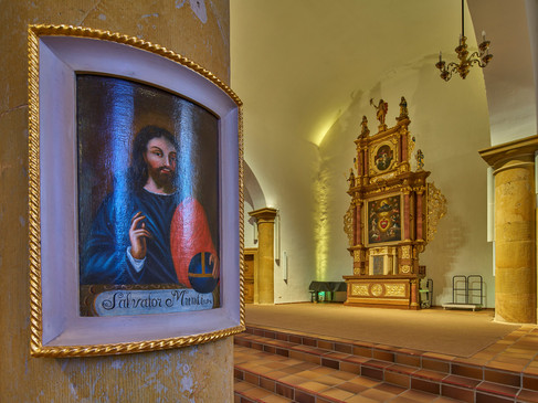 Florales Altargemälde neben Holzaltar in heller, gewölbter Kirche.