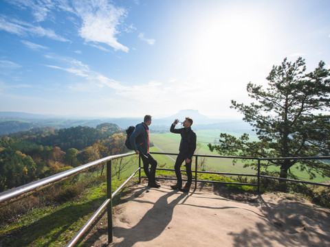 Uitzicht vanaf de Rauenstein uitkijkpost Zwei Männer stehen auf einem Aussichtspunkt mit Geländer, einer trinkt aus einer Flasche. Im Hintergrund eine weite Landschaft und blauer Himmel.