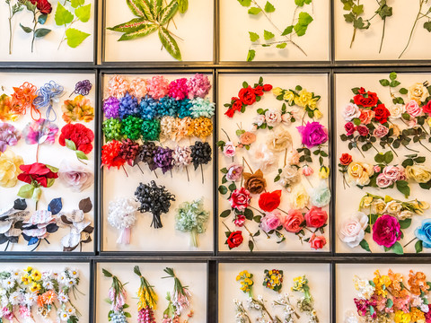 German artificial flower Sebnitz Verschiedene bunte künstliche Blumen und Blätter sind in einem Raster angeordnet, darunter Rosen, Gänseblümchen und Hortensien in lebhaften Farben.