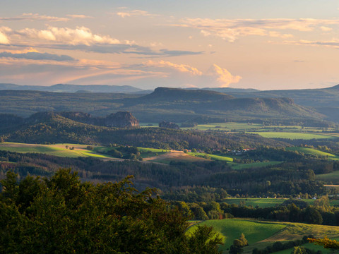 Blick vom Ungerberg Weite Landschaft mit sanften Hügeln und Wäldern im Abendlicht, unter einem Himmel mit pastellfarbenen Wolken.