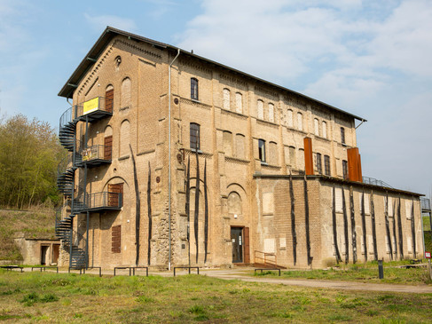Historisches Backsteingebäude der Gedenkstätte Augustaschacht, umgeben von Bäumen und offener Wiese.