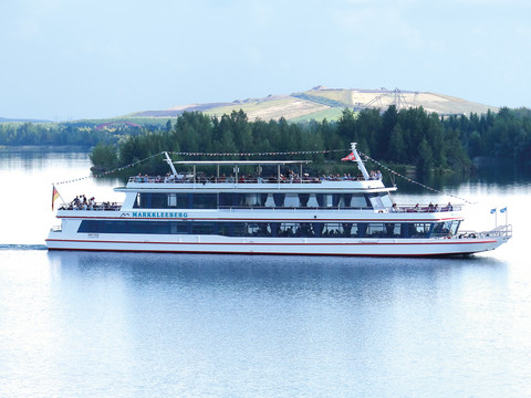 FMS Markkleeberg 2023.jpg Ausflugsschiff FMS Markkleeberg auf ruhigem See, umgeben von grünen Ufern und sanften Hügeln.Excursion boat FMS Markkleeberg on a calm lake, surrounded by green shores and rolling hills.Výletní loď FMS Markkleeberg na klidném jezeře, obklopeném zelenými břehy a kopci.Łódź wycieczkowa FMS Markkleeberg na spokojnym jeziorze, otoczonym zielonymi brzegami i falistymi wzgórzami.Excursieboot FMS Markkleeberg op een rustig meer, omgeven door groene oevers en glooiende heuvels.Barca da escursione FMS Markkleeberg su un lago tranquillo, circondato da rive verdi e dolci colline.