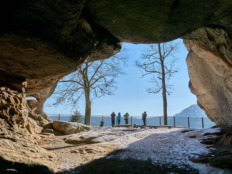 Blick durch den Sandsteinbogen Kuhstall und auf mehreren Personen, die an einem Geländer stehen; klare, sonnige Atmosphäre.