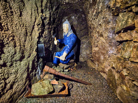 in the Marie Louise Stolln visitor mine Copryright Marko Förster Ein Bergmann in traditioneller Kleidung kniet in einer engen, steinigen Mine, umgeben von Geröll.