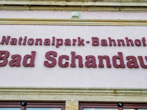 Rote Schrift auf rosa Wand mit der Aufschrift "Nationalpark-Bahnhof Bad Schandau".Red lettering on a pink wall with the inscription "Nationalpark-Bahnhof Bad Schandau".Červený nápis na růžové zdi s nápisem "Nádraží Národního parku Bad Schandau".Czerwony napis na różowej ścianie z napisem "Bad Schandau National Park railway station".Rode letters op een roze muur met het opschrift "Bad Schandau National Park railway station".Scritta rossa su un muro rosa con la scritta "Stazione ferroviaria del Parco Nazionale di Bad Schandau".