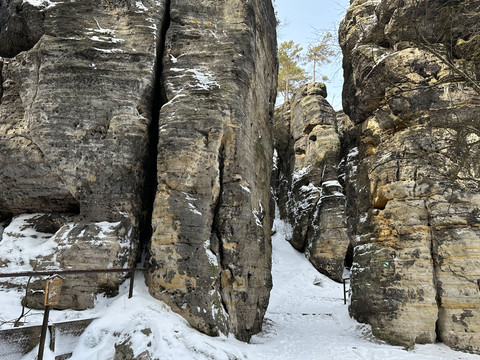 Tyssaer Wände im Winter Verschneite Felsformationen mit schmalem Pfad dazwischen, umgeben von kahlen Bäumen und blauem Himmel.Snow-covered rock formations with a narrow path between them, surrounded by bare trees and a blue sky.Zasněžené skalní útvary s úzkou stezkou mezi nimi, obklopené holými stromy a modrou oblohou.Pokryte śniegiem formacje skalne z wąską ścieżką między nimi, otoczone nagimi drzewami i błękitnym niebem.Besneeuwde rotsformaties met een smal pad ertussen, omringd door kale bomen en een blauwe lucht.Formazioni rocciose innevate con uno stretto sentiero tra di esse, circondate da alberi spogli e da un cielo azzurro.