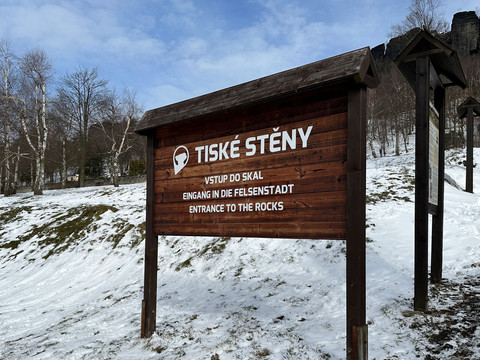 Schild zu den Tyssaer Wänden Holzschild mit der Aufschrift "Tiské Stěny" vor schneebedecktem Boden und kahlen Bäumen, blauer Himmel im Hintergrund.Wooden sign with the inscription "Tiské Stěny" in front of snow-covered ground and bare trees, blue sky in the background.Dřevěná cedule s nápisem "Tiské Stěny" před zasněženou zemí a holými stromy, v pozadí modrá obloha.Drewniana tablica z napisem "Tiské Stěny" na tle ośnieżonej ziemi i nagich drzew, w tle błękitne niebo.Houten bord met het opschrift "Tiské Stěny" voor een besneeuwde grond en kale bomen, blauwe lucht op de achtergrond.Cartello in legno con la scritta "Tiské Stěny" davanti a un terreno innevato e ad alberi spogli, con il cielo azzurro sullo sfondo.