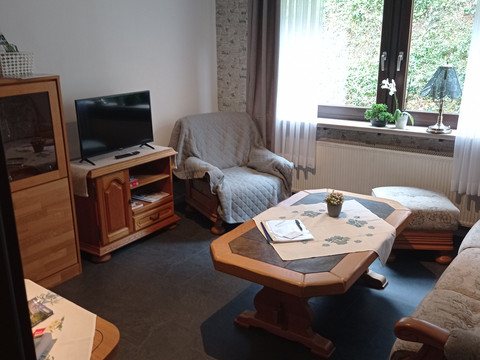 IMG_20230412_143803.jpg Wohnzimmer mit gemütlichen Polstermöbeln, TV, Holztisch, Fenster mit weißem Vorhang und Gartenblick.