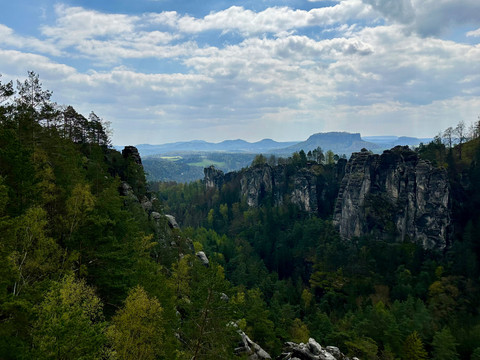Blick auf eine bewaldete Felslandschaft mit steilen Klippen unter einem bewölkten Himmel, im Hintergrund sind sanfte Hügel zu sehen.View of a wooded rocky landscape with steep cliffs under a cloudy sky, with rolling hills in the background.Pohled na zalesněnou skalnatou krajinu se strmými útesy pod zataženou oblohou, v pozadí kopce.Widok zalesionego skalistego krajobrazu ze stromymi klifami pod zachmurzonym niebem, z falistymi wzgórzami w tle.Uitzicht op een bebost rotslandschap met steile kliffen onder een bewolkte hemel, met glooiende heuvels op de achtergrond.Vista di un paesaggio roccioso boscoso con ripide scogliere sotto un cielo nuvoloso, con dolci colline sullo sfondo.