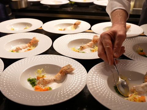 Bergische Genusstage Ein Küchenchef arrangiert kunstvoll Garnelen auf elegant servierten Tellern in einer Gourmetküche.