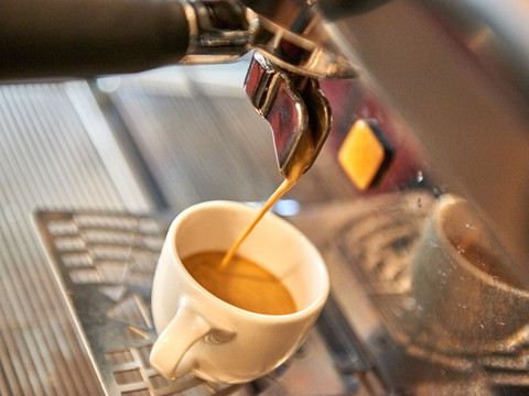 Espresso fließt aus einer Siebträgermaschine in eine weiße Tasse, die auf einem Metallgitter steht.