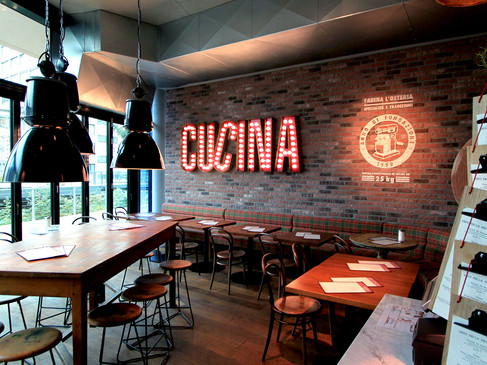 Ein modernes Restaurant mit industriellem Dekor; Holzmöbel, Ziegelwand und große Leuchtreklame "Cucina".