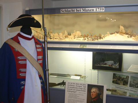 Mannequin in historischer Uniform mit Dreispitz vor einem Diorama der Schlacht bei Maxen 1759, umgeben von Infotafeln und Bildern.