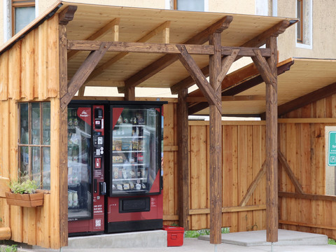 Proviantomat in Pfaffendorf Ein roter Verkaufsautomat steht unter einem hölzernen Unterstand neben einem Gebäude, umgeben von Holzwänden und einem Schild mit der Aufschrift "Spielplatz".A red vending machine stands under a wooden shelter next to a building, surrounded by wooden walls and a sign saying "Playground".Pod dřevěným přístřeškem vedle budovy, obklopené dřevěnými stěnami a nápisem "Dětské hřiště", stojí červený automat.Czerwony automat stoi pod drewnianą wiatą obok budynku, otoczony drewnianymi ścianami i tabliczką z napisem "Plac zabaw".Een rode automaat staat onder een houten afdak naast een gebouw, omringd door houten muren en een bord met de tekst "Playground".Un distributore automatico rosso si trova sotto una tettoia di legno accanto a un edificio, circondato da pareti di legno e da un cartello con la scritta "Parco giochi".