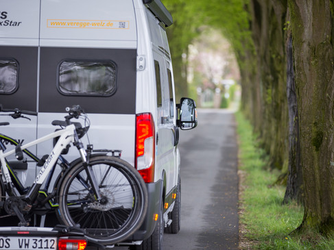 Camperplaatsen in de regio Osnabrück Ein Wohnmobil mit Fahrradträger fährt auf einer von Bäumen gesäumten Landstraße entlang.