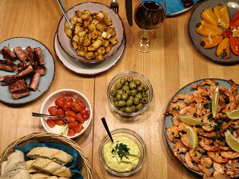 Vielfältige Tapasauswahl mit gegrilltem Fleisch, Garnelen, buntem Gemüse, Brot, Oliven und Wein.
