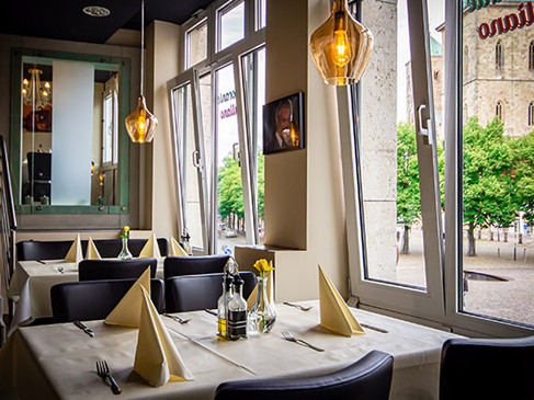 Ein helles Restaurant mit eleganten Tischdekorationen, großen Fenstern und moderner Beleuchtung.