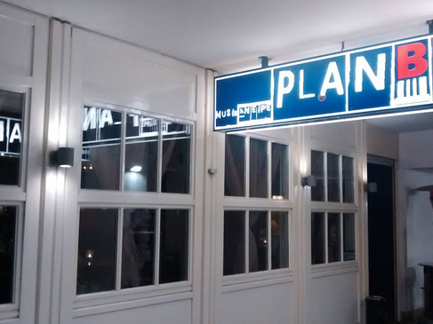Ein beleuchtetes Schild mit der Aufschrift "Plan B" über der Eingangstür eines Gebäudes bei Nacht.