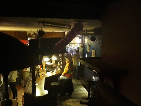 Eine stimmungsvolle Bar mit Holztresen, gedämpfter Beleuchtung und mehreren Personen, die sich unterhalten.