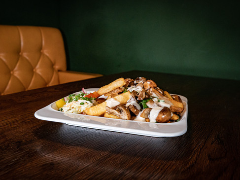 Ein Teller mit Pommes, Pilzen und Saucen, angerichtet auf einem Holztisch in einem dunkelgrünen Raum.