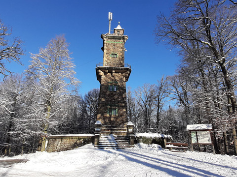 A stone observation tower in the snowy forest, surrounded by snow-covered trees under a clear blue sky.