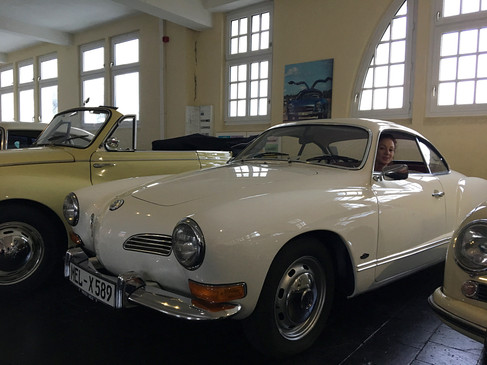Frau sitzt lächelnd in einem weißen Oldtimer im Automuseum Melle, neben weiteren klassischen Autos.