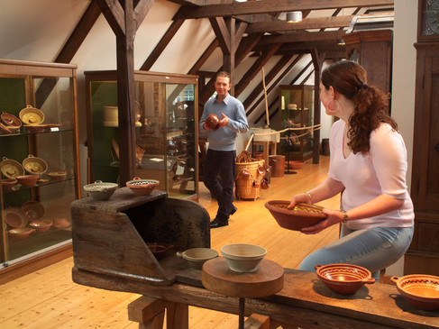 Menschen in traditionell eingerichteter Töpferei, betrachten Keramikobjekte.