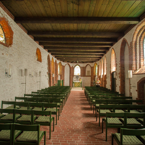 bispingen-kirche-innenraum Die Bispingen Kirche im Inneren zeigt eine Reihe von Holzbänken, umgeben von leuchtenden Buntglasfenstern und einem von Holzdeckenbalken überspannten Raum, der einen warmen, einladenden Charakter verleiht.