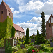 St-Johannes Kirche Die St.-Johannes-Kirche erhebt sich majestätisch über den gepflegten Kirchhof mit blühenden Beeten und Grabsteinen. Der Turm ist mit Efeu bewachsen, was ihm ein malerisches Aussehen verleiht.