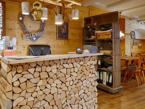 Ontvangstruimte met rustieke balie van boomstammen, versierd met een hart en een bordje "Welkom"; warme, uitnodigende sfeer.