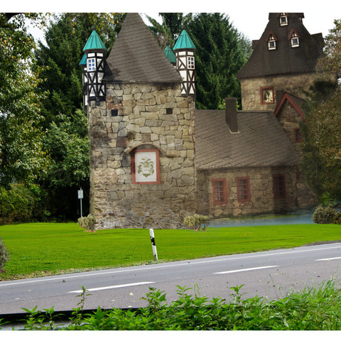Burgruine Herrenbröl Historisches Steinhaus mit zwei Türmen und grünen Dächern, umgeben von Bäumen und Wiesen.