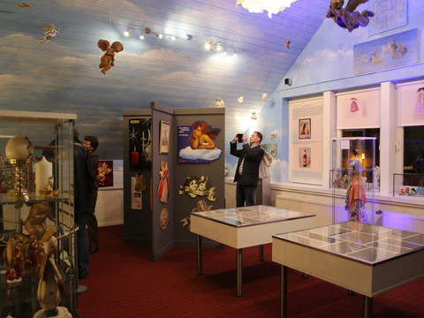 Blick in das Museum Besucher erkunden ein Museum mit Engelfiguren und Kunst in einem Raum mit himmelblauer Decke.