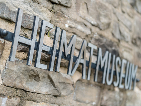 Hückeswagen <p>Metallschild "Heimatmuseum" an einer alten Steinmauer in Hückeswagen, unscharfer Hintergrund.</p>